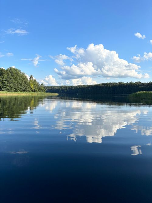 Free Peaceful summer lake scene with clear reflections and vibrant blue sky. Stock Photo
