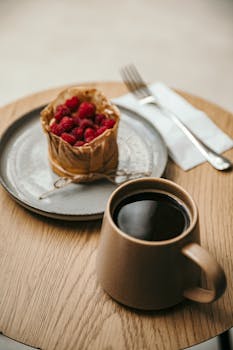 A cozy coffee mug and raspberry pastry on a wooden table set a warm and inviting scene.