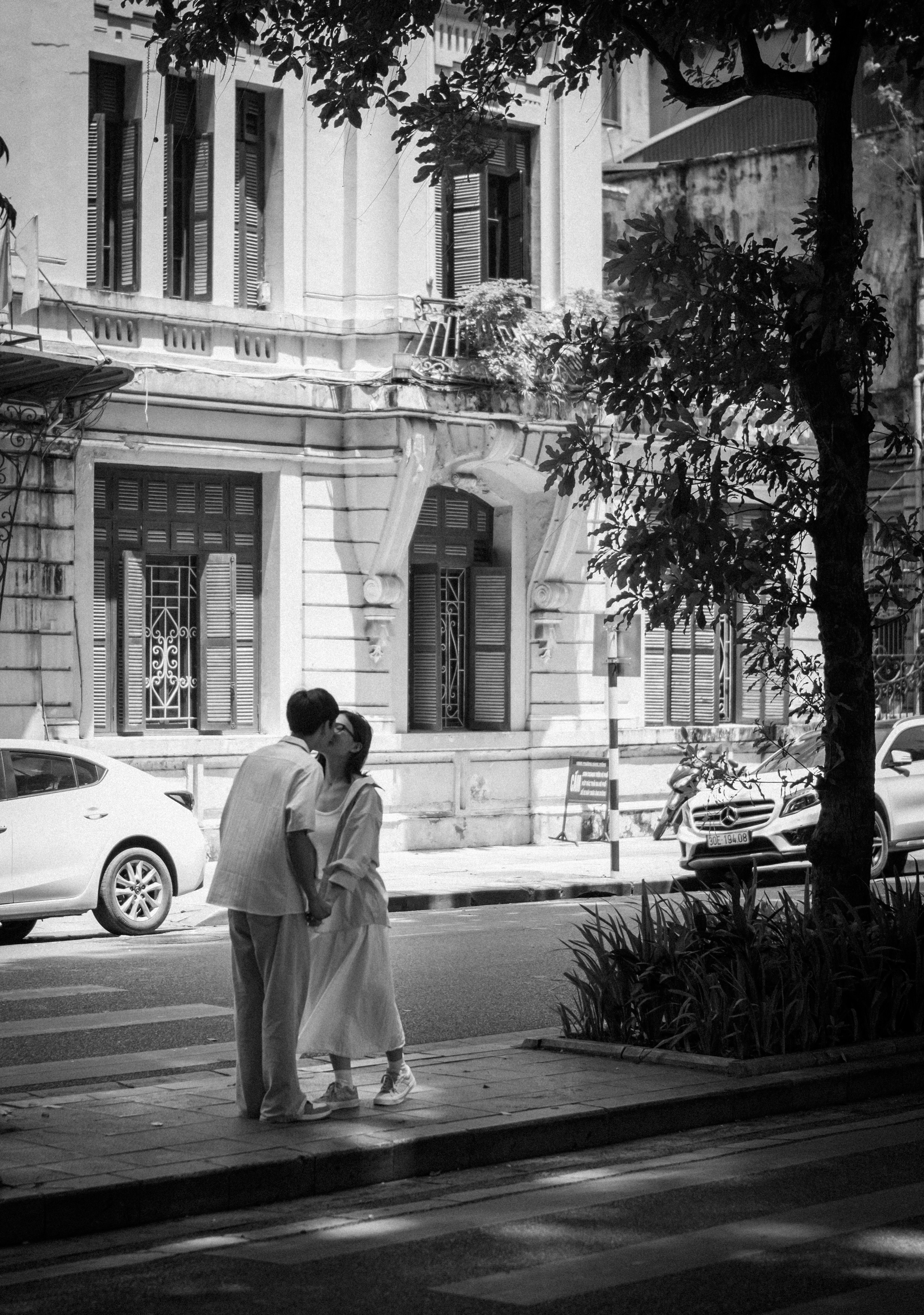 A romantic moment of a couple embracing on a street in Hanoi, Vietnam, captured in classic black and white.