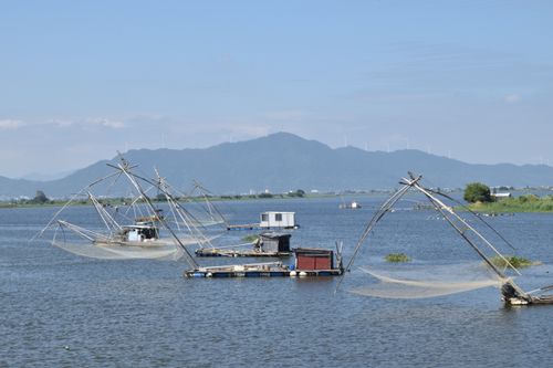 Free Traditional fishing nets on a calm lake with mountains and wind turbines in the background. Stock Photo