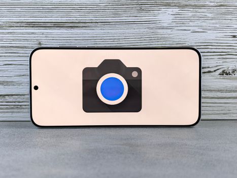 A smartphone with a camera icon displayed on a screen set against a wooden background.