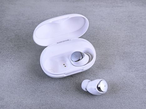 High-quality image of white wireless earbuds and charging case on a textured surface.
