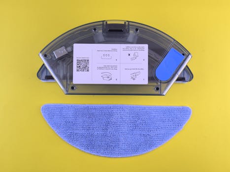 Cleaning robot water tank and mop on yellow backdrop, showcasing household appliance detail.