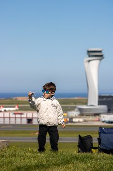 Young boy with toy plane near airport control tower on a sunny day in İstanbul.