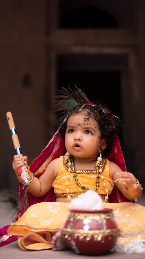 Free Cute baby dressed in vibrant traditional Indian attire, holding a flute with a clay pot nearby. Stock Photo