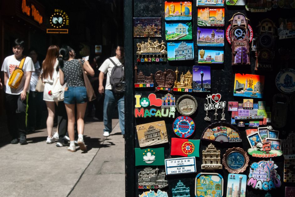 Vibrant collection of Macau-themed souvenirs with pedestrians on a sunny street.