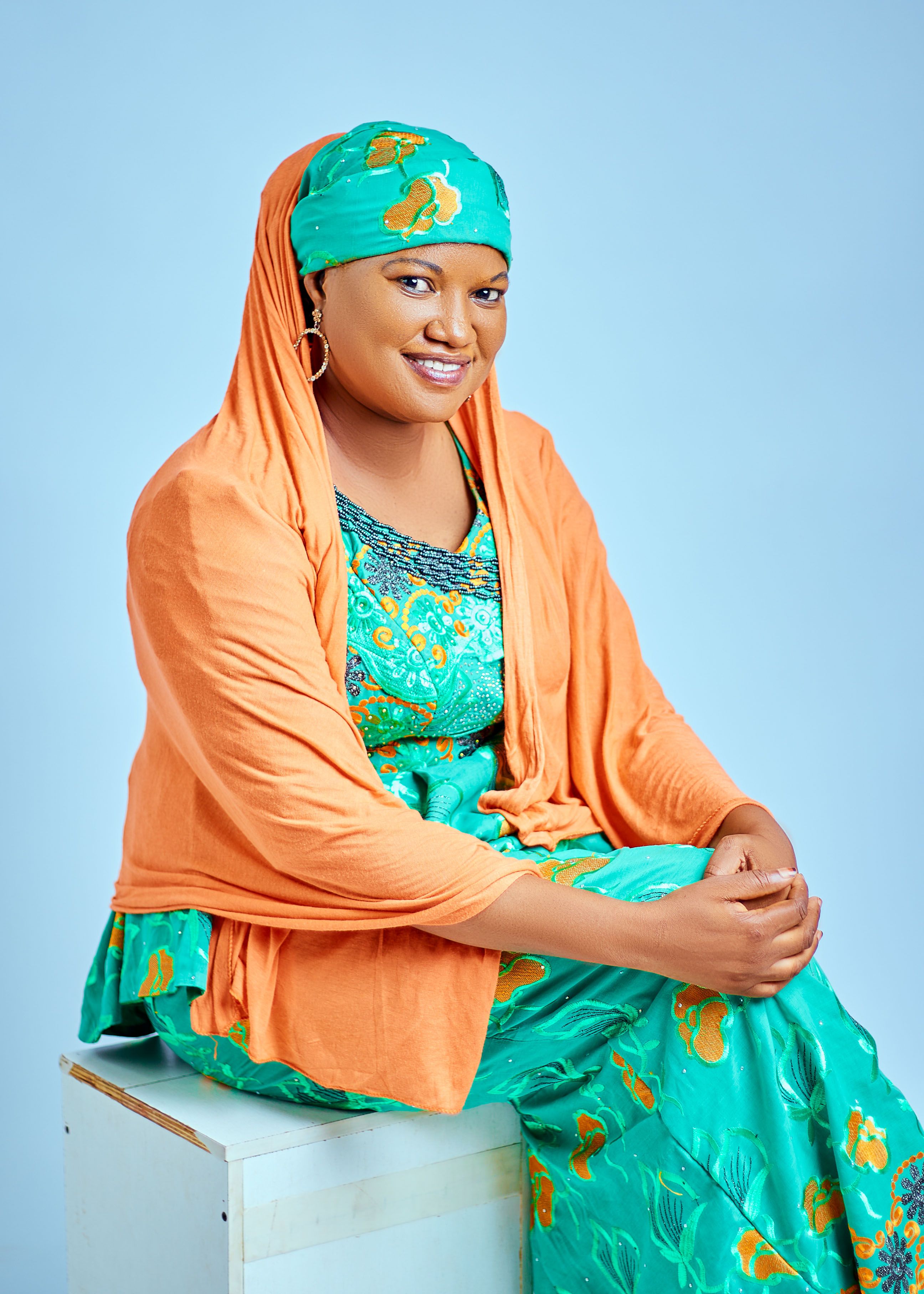 Smiling woman in vibrant traditional attire against a soft blue background, exuding warmth.