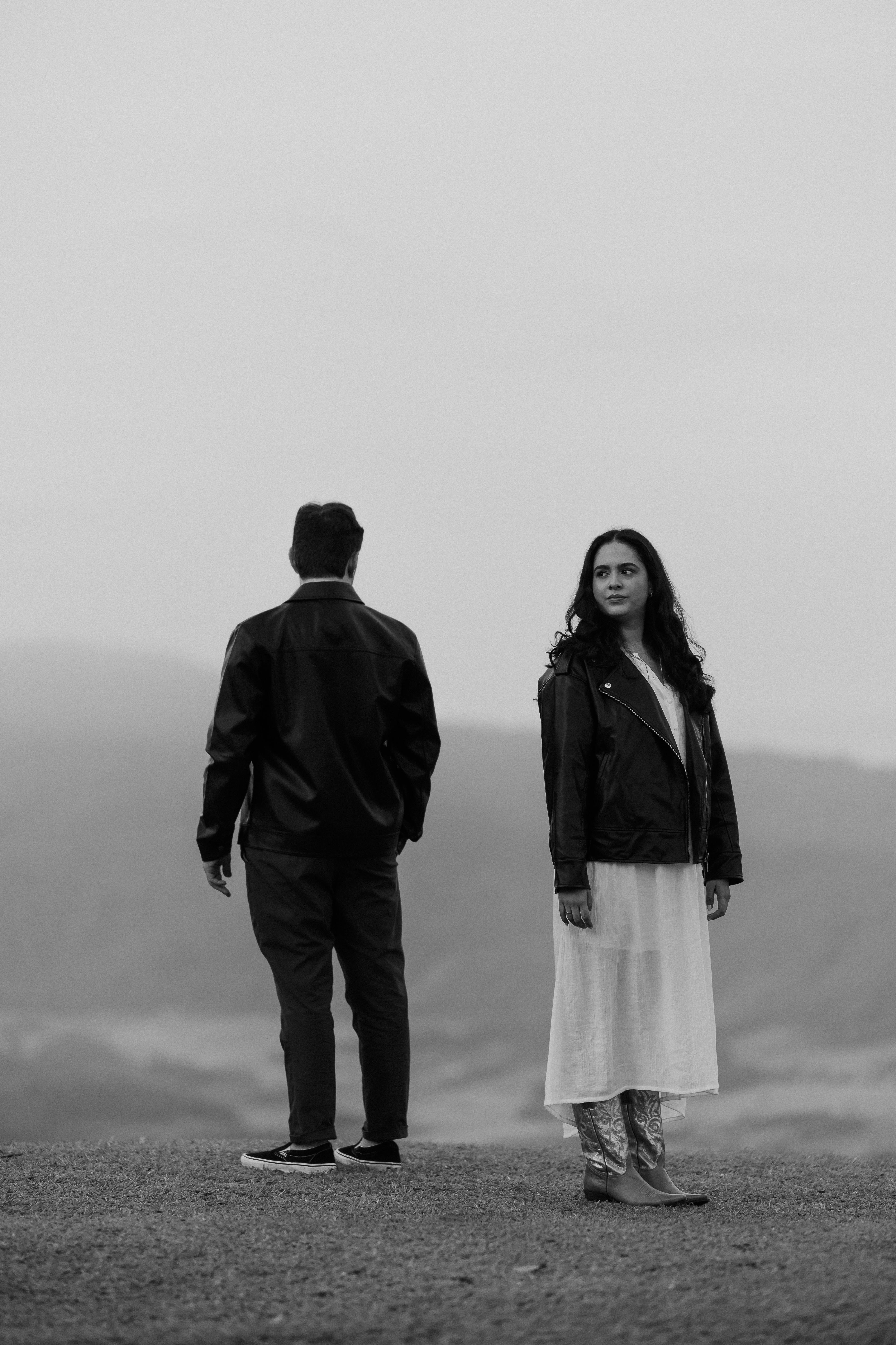 A couple standing apart in a serene outdoor setting, captured in black and white.