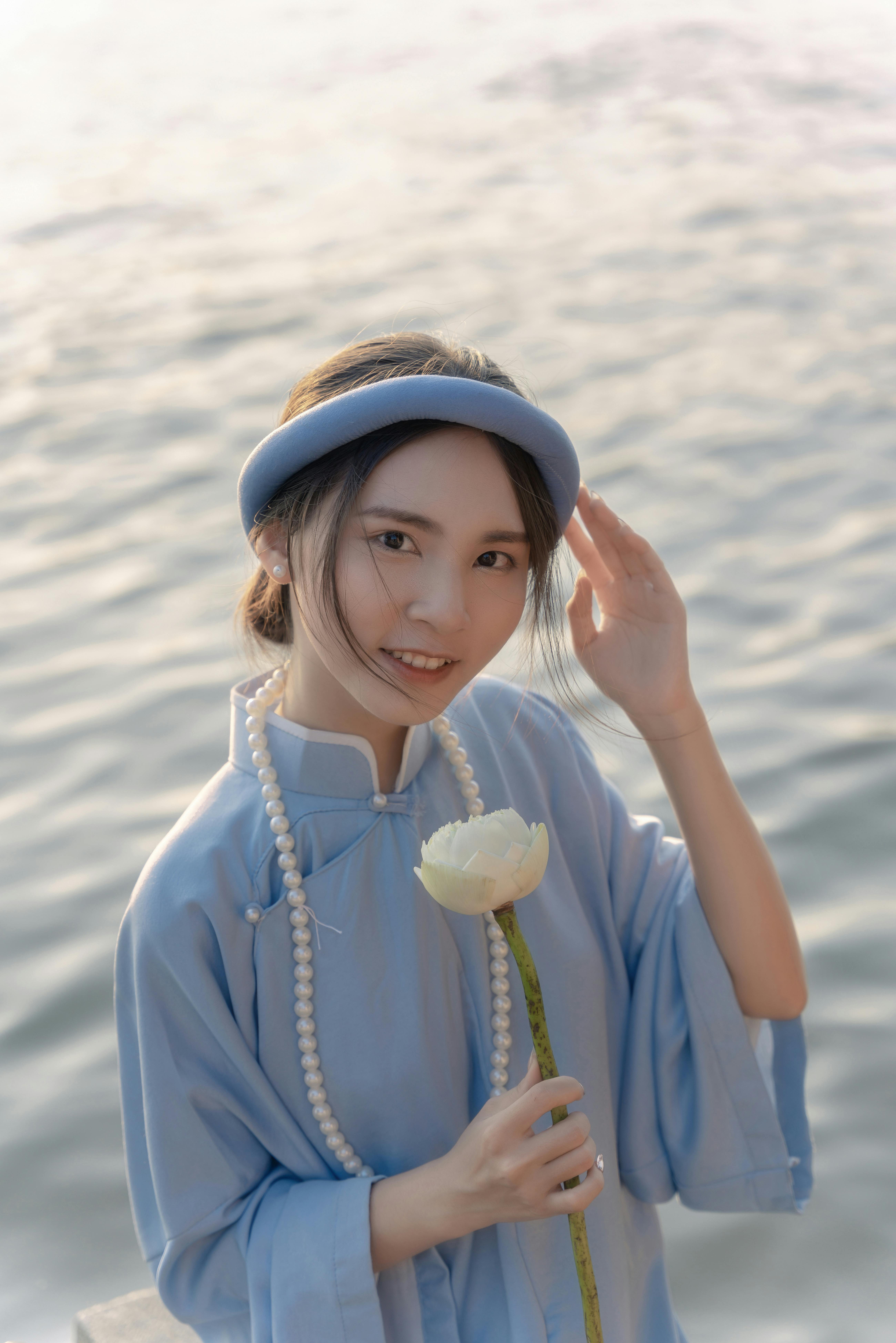 A serene portrait of a woman in a blue traditional outfit with a white flower by the water.