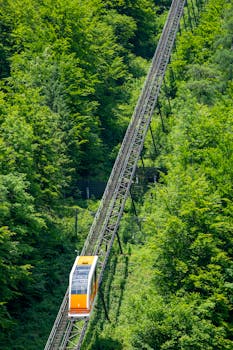 A vibrant orange funicular train ascends through dense green forest on a steep track.