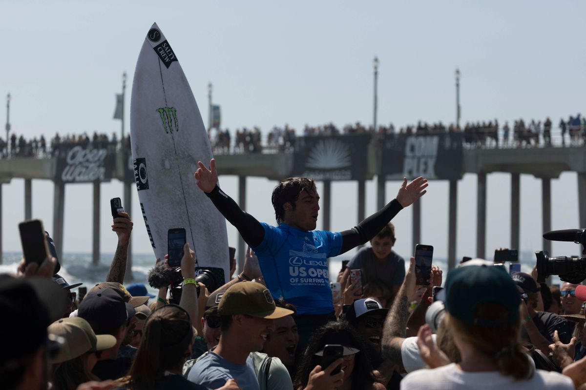 Surfer celebrating a competition win surrounded by a cheering crowd at a beach surf event