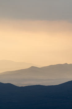 A calming view of layered mountains during sunset with warm tones and a tranquil atmosphere.