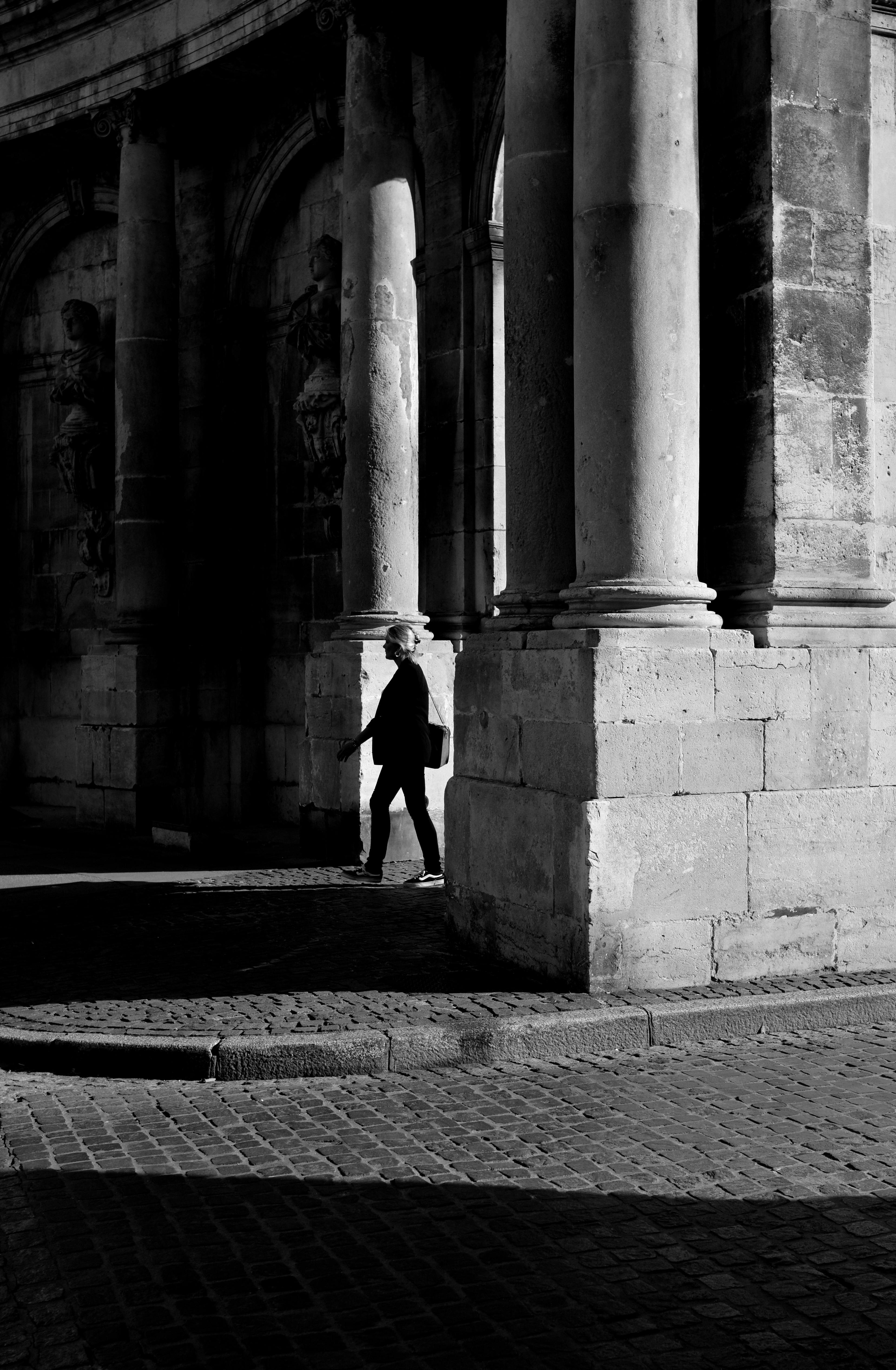 A person walks near grand stone arches in France. Dramatic shadows create contrast in this urban scene.