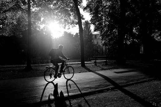 A cyclist rides through a scenic park in France at sunset, captured in black and white.