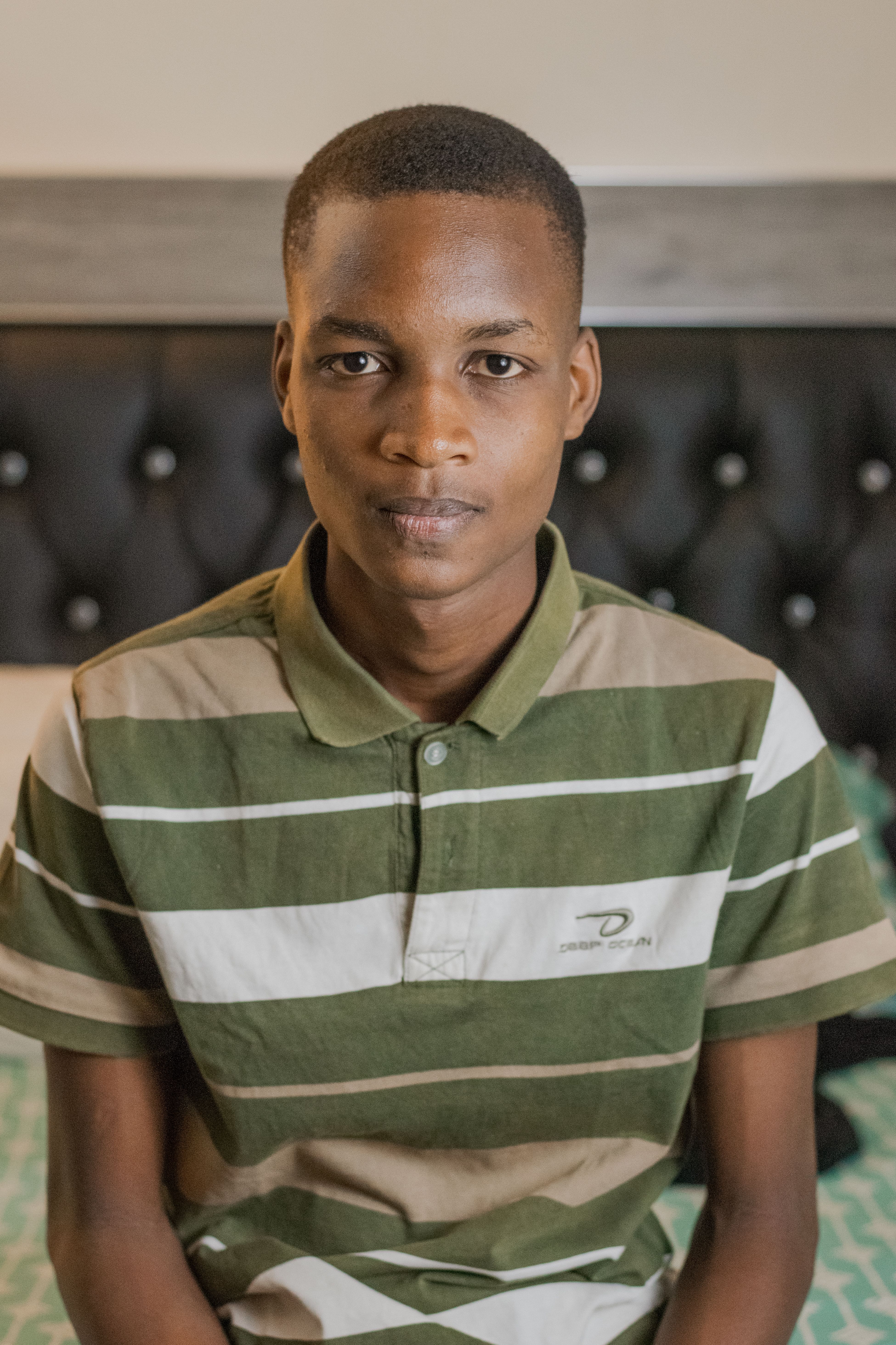 A young adult wearing a green and white striped shirt poses indoors with a neutral expression.