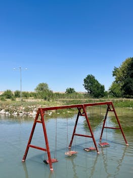 Red swing set standing in calm water under a clear blue sky in Çifteler, Türkiye.