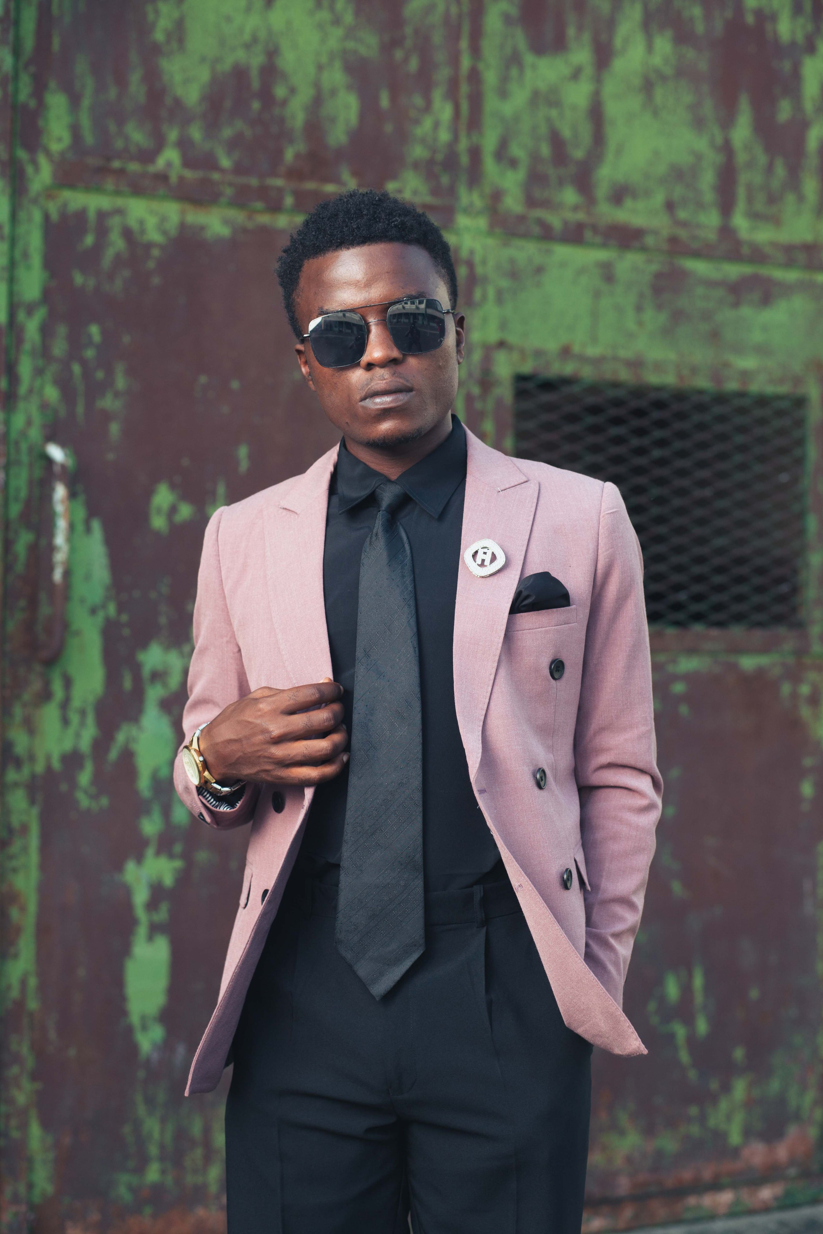 Homem negro elegante usando um blazer rosa e óculos de sol, posando confiante ao ar livre.