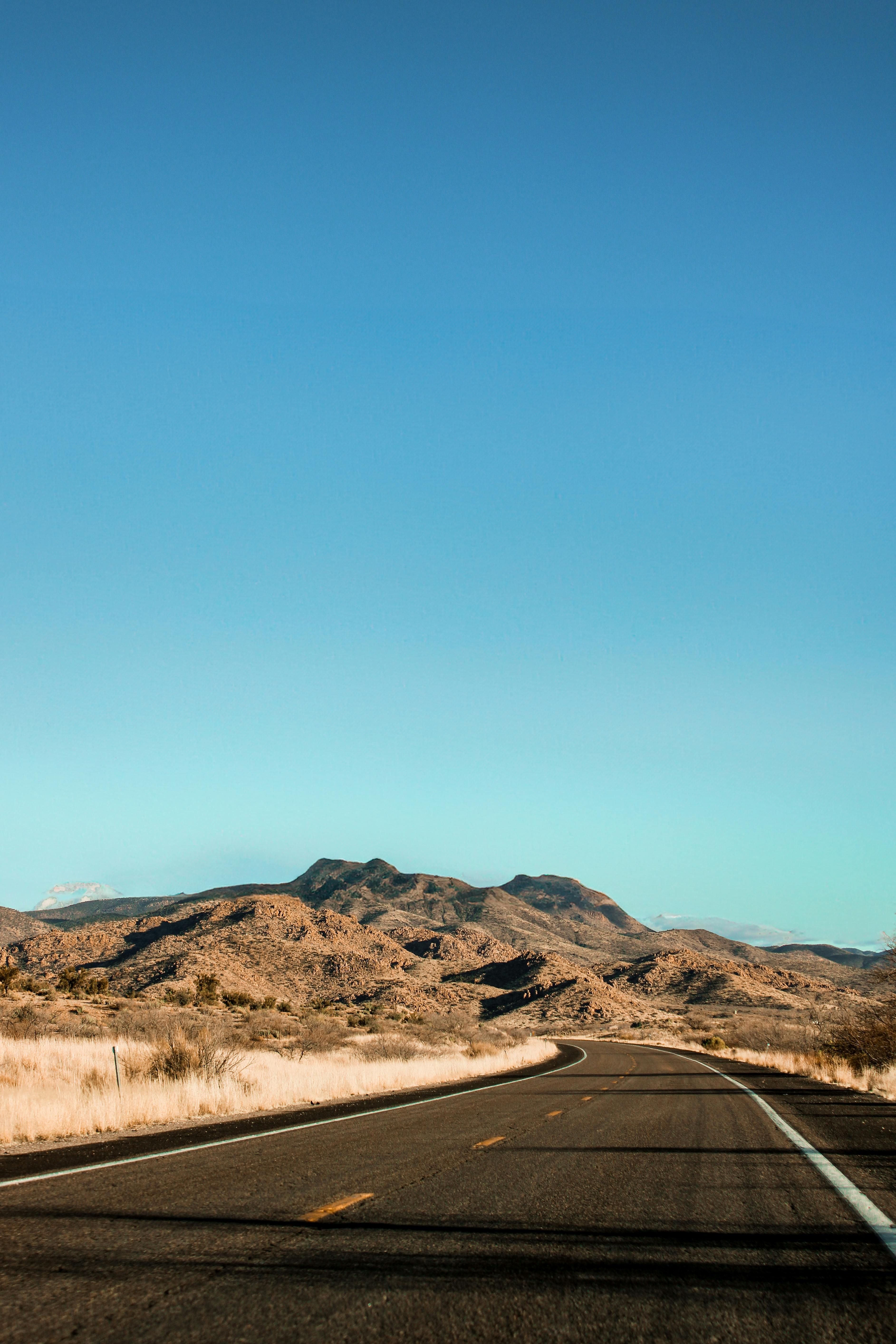 A picturesque view of a highway traversing the arid Arizona desert with mountains in the distance.
