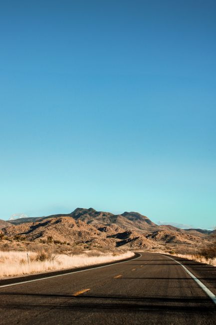 A picturesque view of a highway traversing the arid Arizona desert with mountains in the distance.