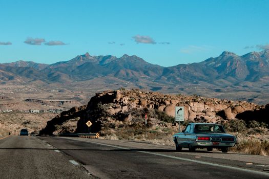 Vintage car travels along a scenic highway in the Arizona desert with majestic mountain views.
