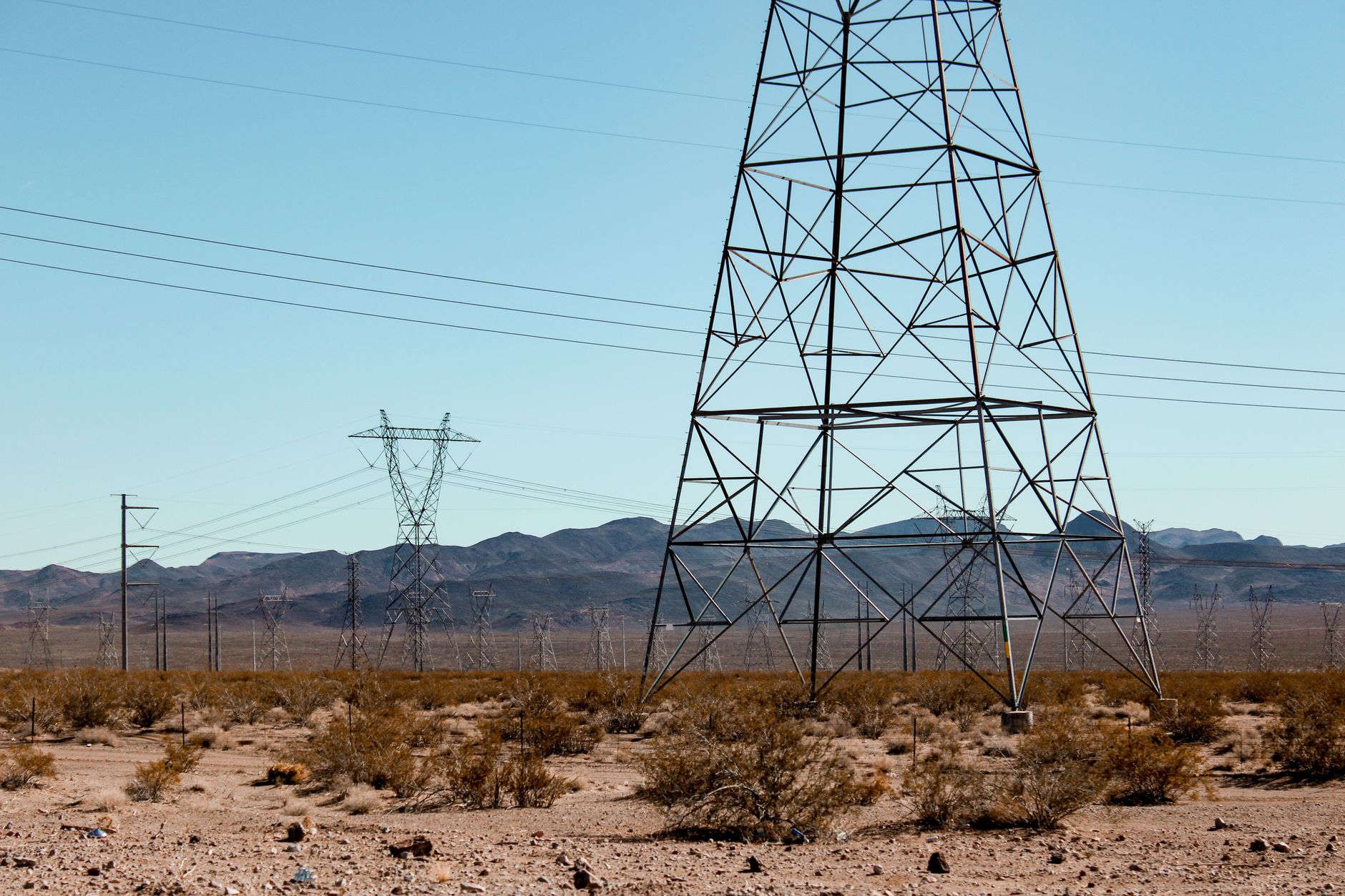 High voltage power lines stand tall in the vast Nevada desert under a clear blue sky.