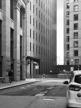 Black and white photo of a quiet urban street lined with tall buildings, ideal for cityscape themes.