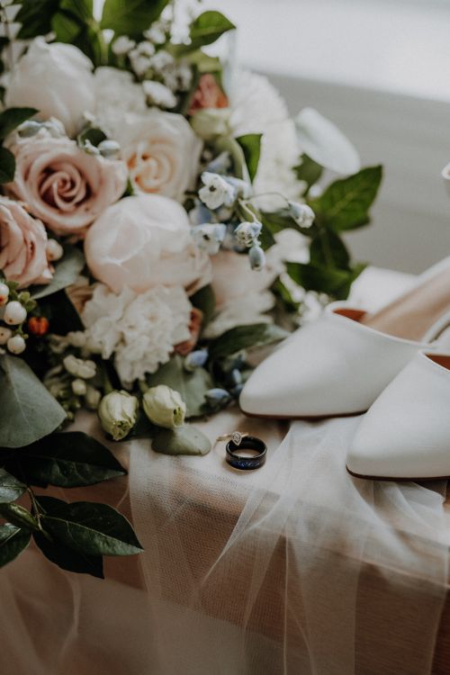 Free Close-up of a wedding bouquet with roses, rings, and elegant white shoes, perfect for bridal themes. Stock Photo