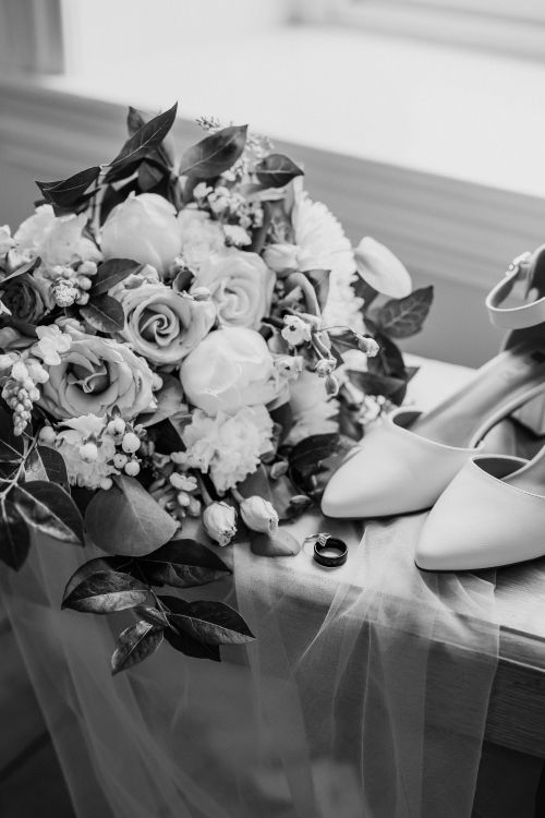 Free Black and white photo of a wedding bouquet, rings, and heels, capturing wedding elegance. Stock Photo