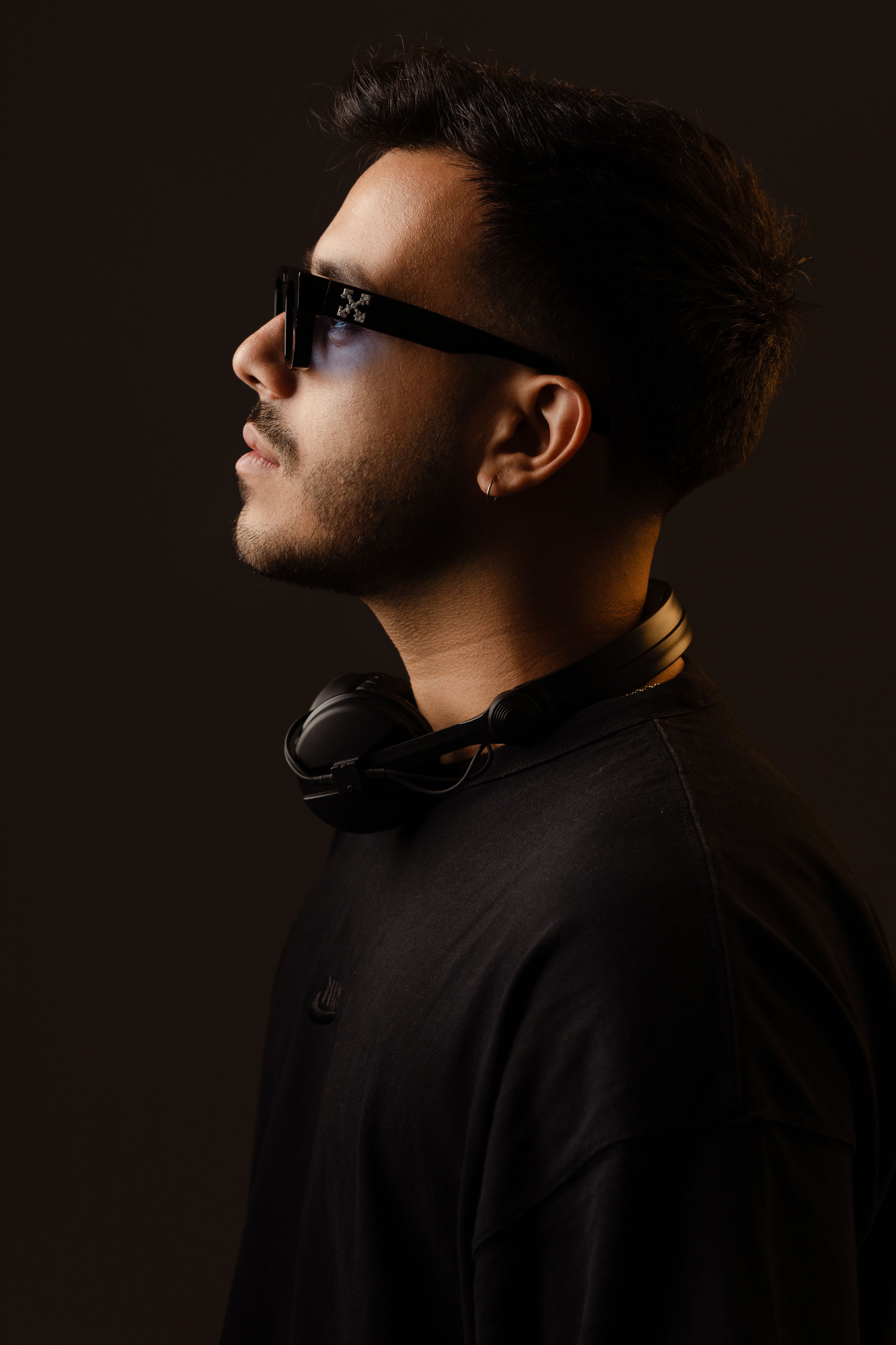 Side profile portrait of man wearing glasses and headphones, set against a dark background.