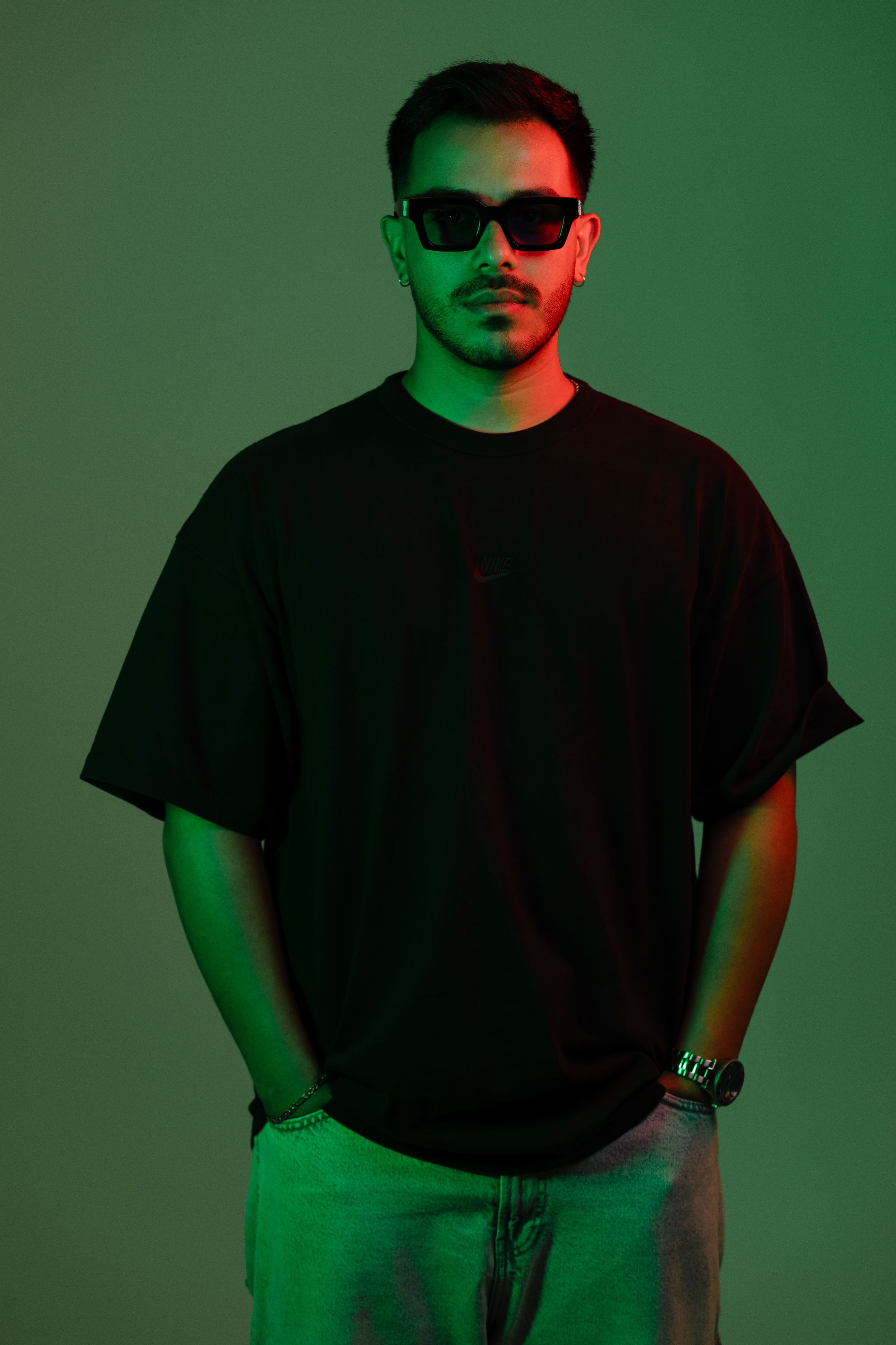 Young man in sunglasses poses confidently under stylish green and red lighting.