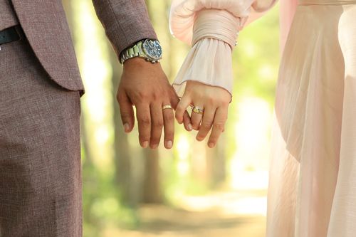 Free Elegant couple holding hands outdoors, showcasing wedding rings and stylish fashion in a bright daylight setting. Stock Photo