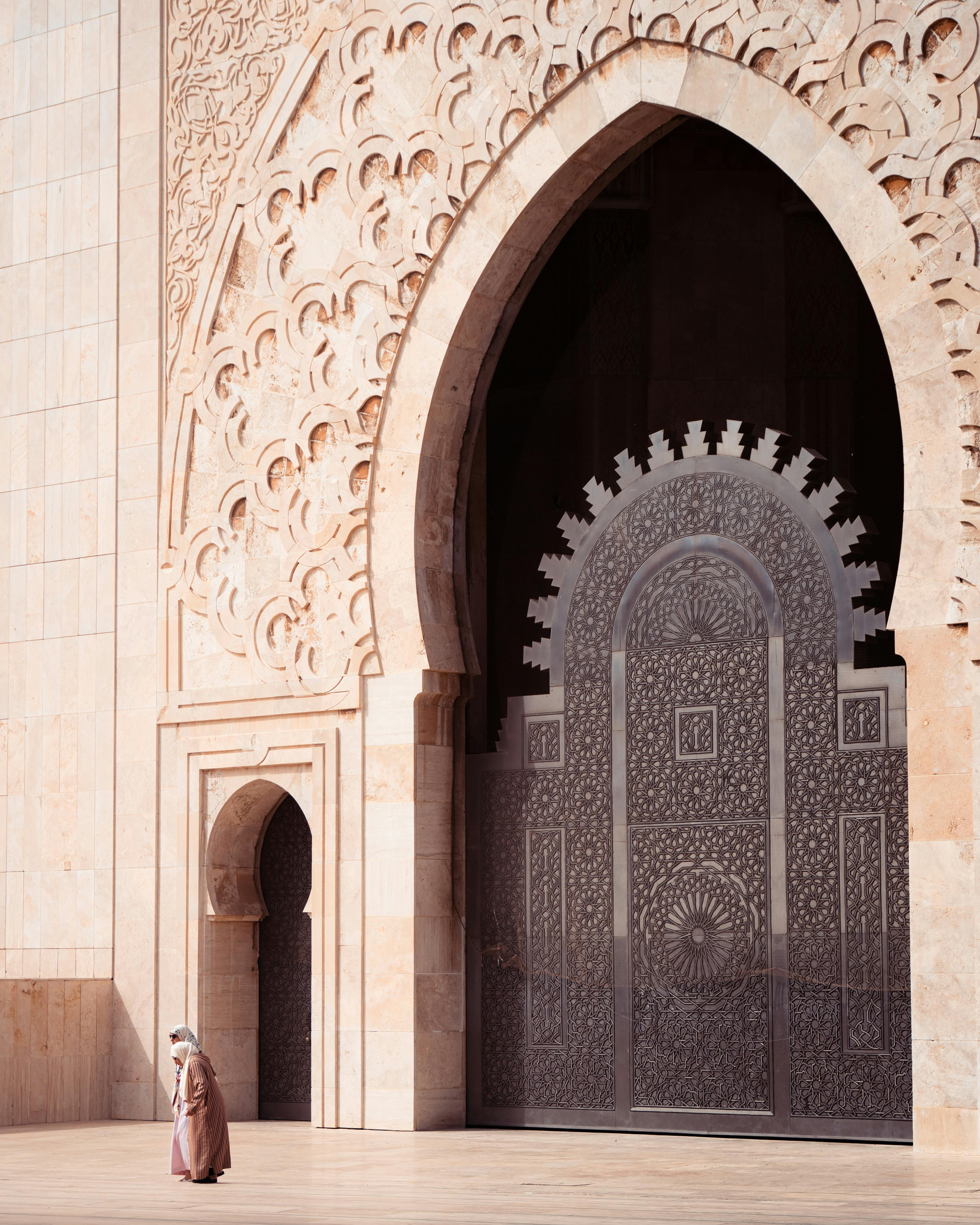A lone figure walks near the intricate entrance of Hassan II Mosque at sunrise, showcasing its stunning architecture.