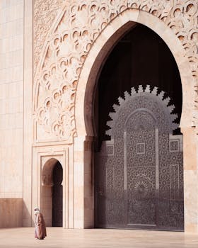 A lone figure walks near the intricate entrance of Hassan II Mosque at sunrise, showcasing its stunning architecture.