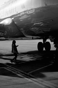 Dramatic black and white silhouette of a traveler approaching a jet on the tarmac.