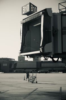 Monochrome image of an airport jet bridge with a worker near a mobile staircase.