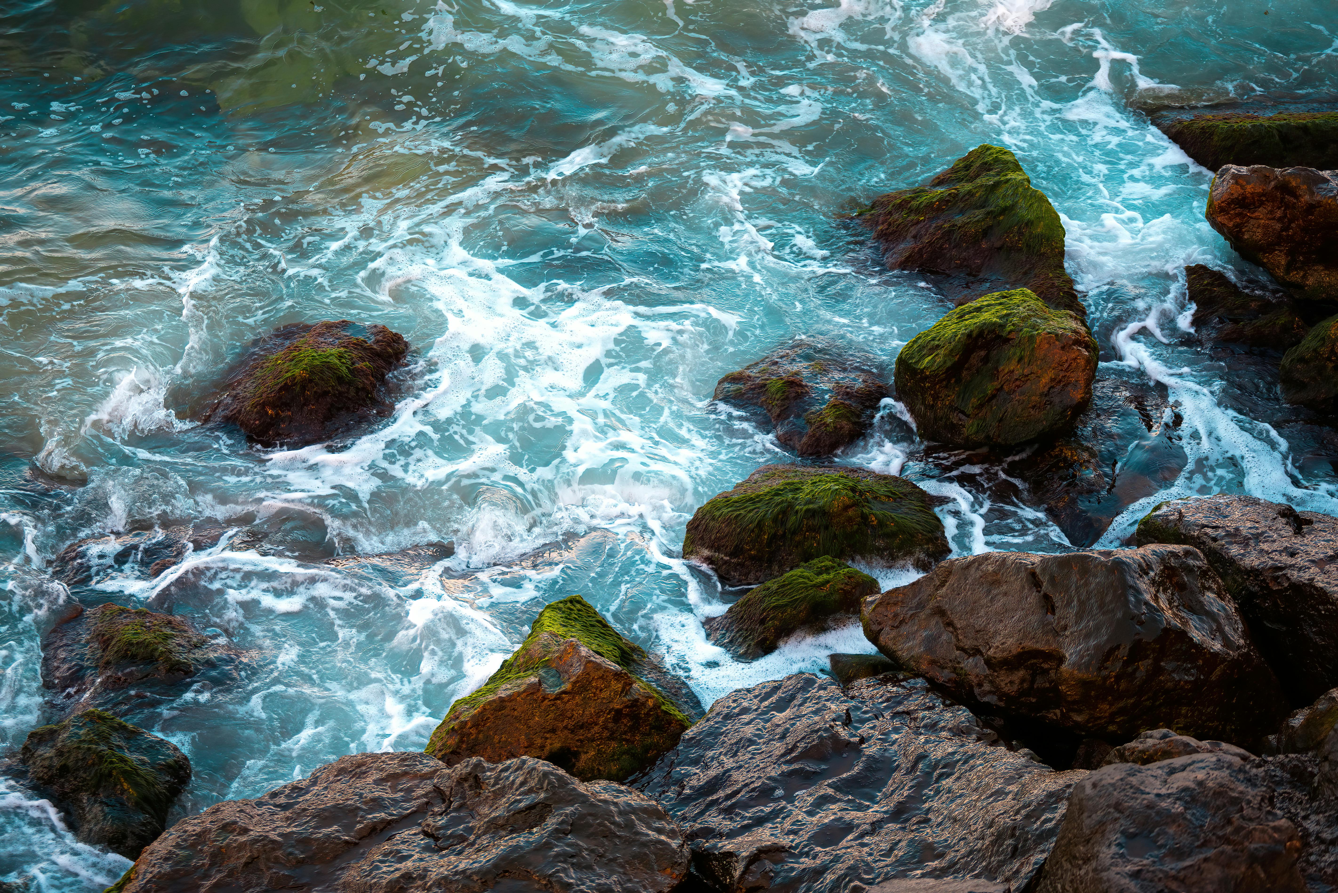Vibrant ocean waves crash against moss-covered rocks in a dynamic seaside scene.