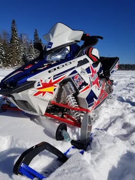 Close-up of a colorful snowmobile in a snowy winter landscape under a bright blue sky.