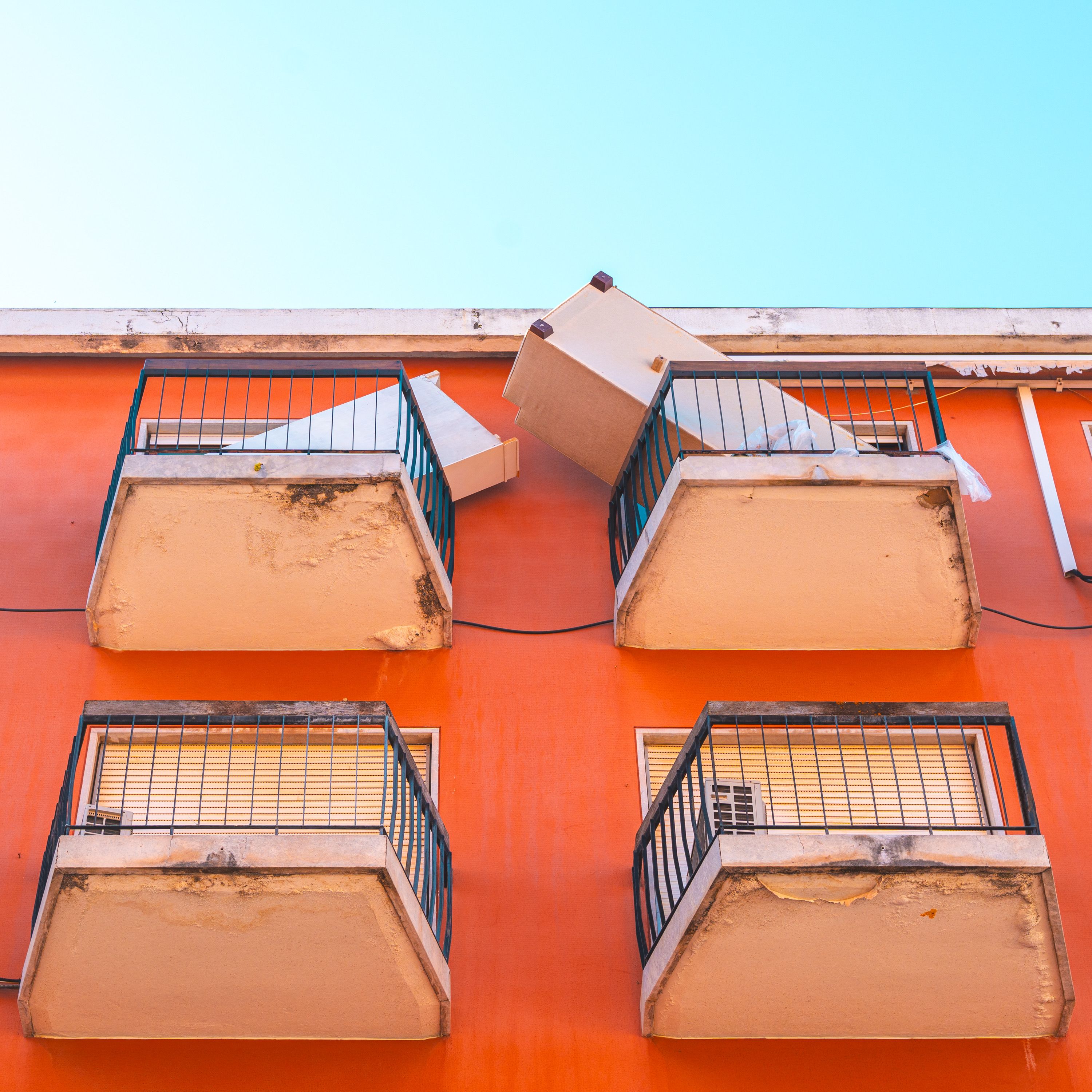 Picture of three balconies with a playful orange facade and clear sky.