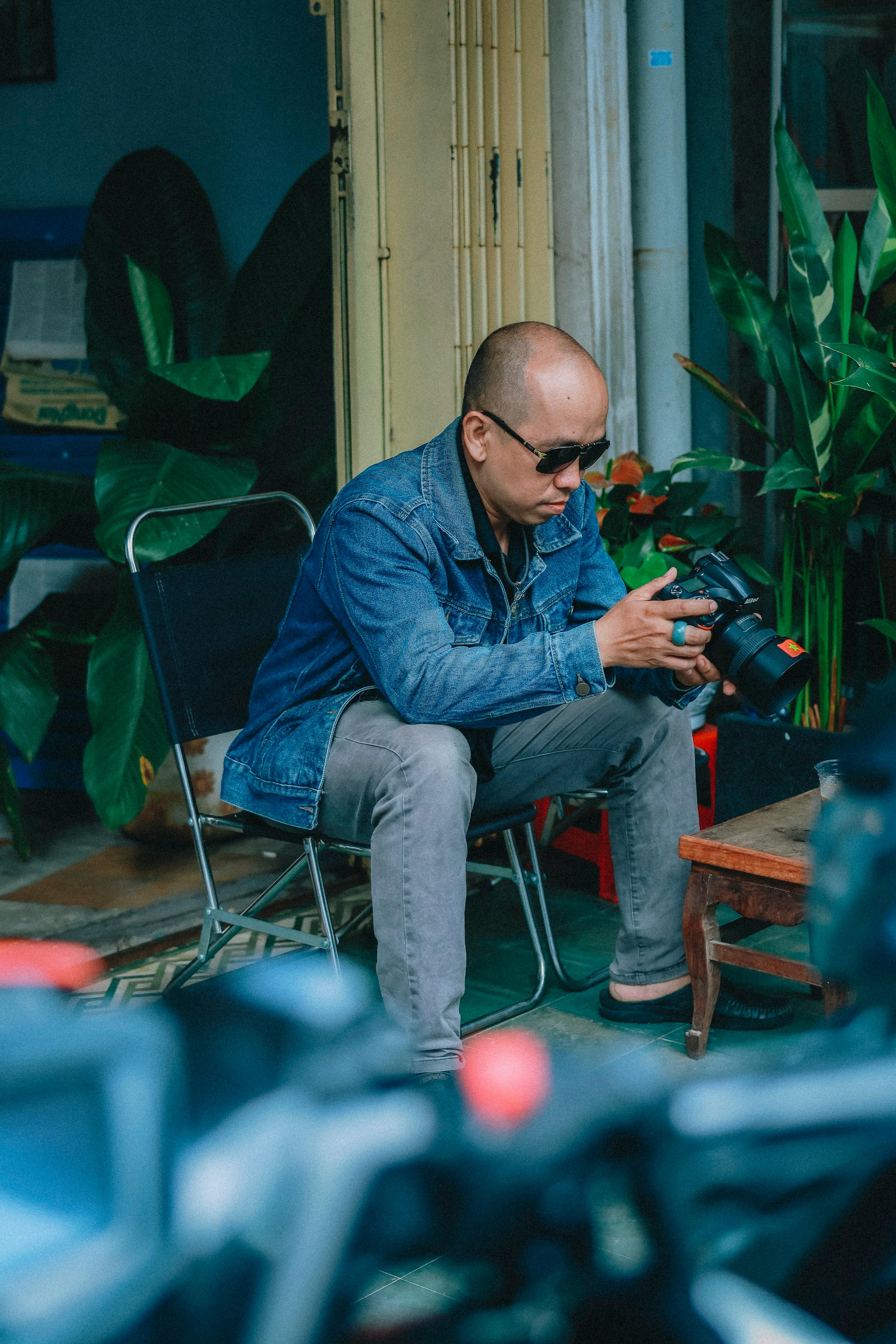 Free Man in denim jacket checking camera settings indoors with plants. Stock Photo