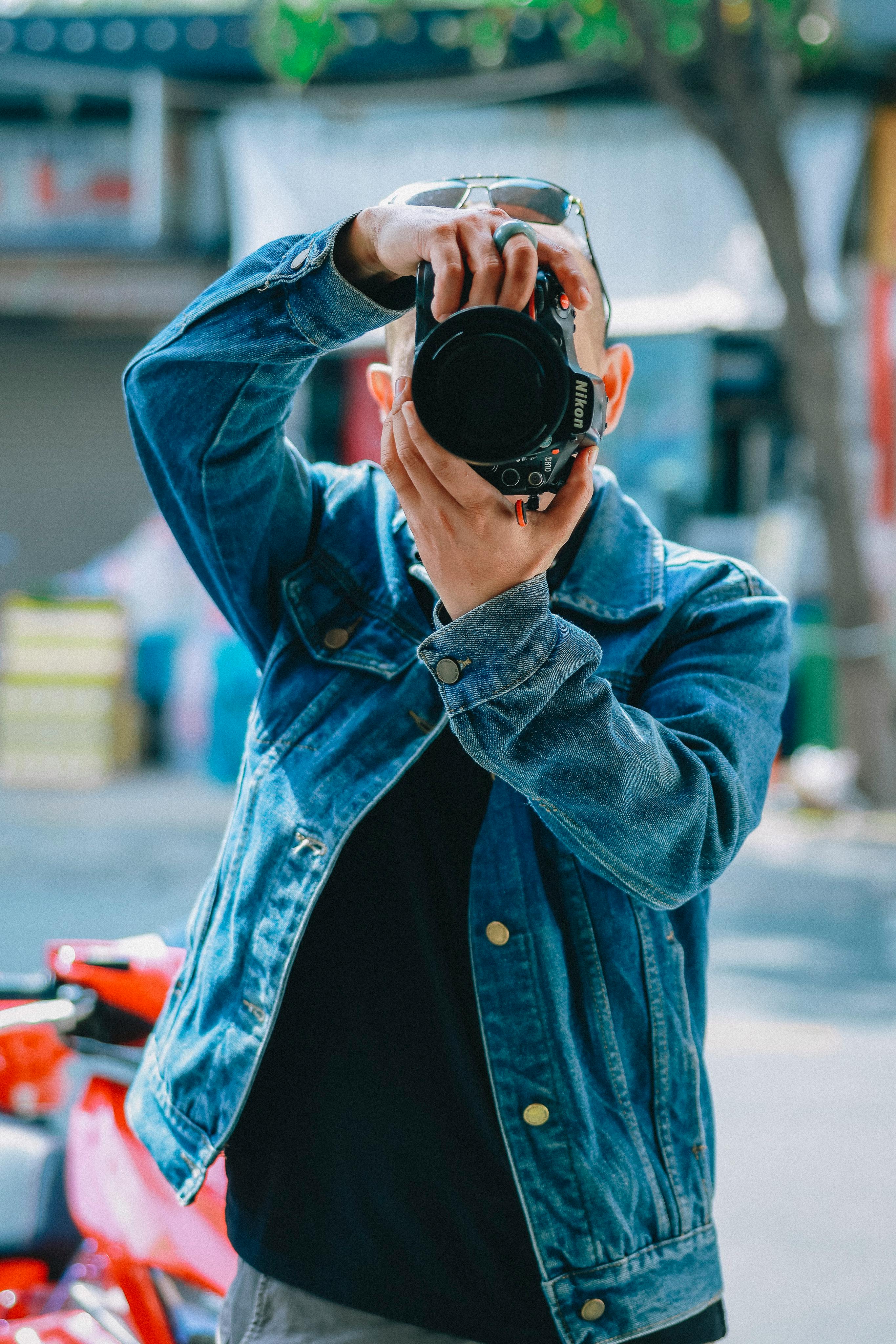 Free A photographer with a camera in denim jacket taking photos outdoors. Stock Photo