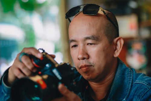 Free Male photographer adjusting camera settings in a bright indoor setting. Stock Photo