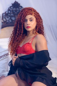 A captivating portrait of a woman with curly red hair in elegant red lingerie, exuding confidence and style.