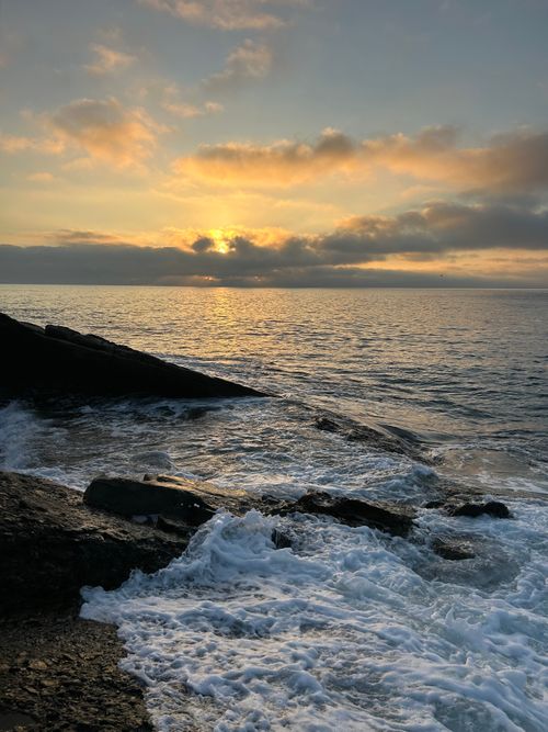 Free Stunning view of a sunrise over a tranquil ocean with waves crashing against rugged rocks. Stock Photo