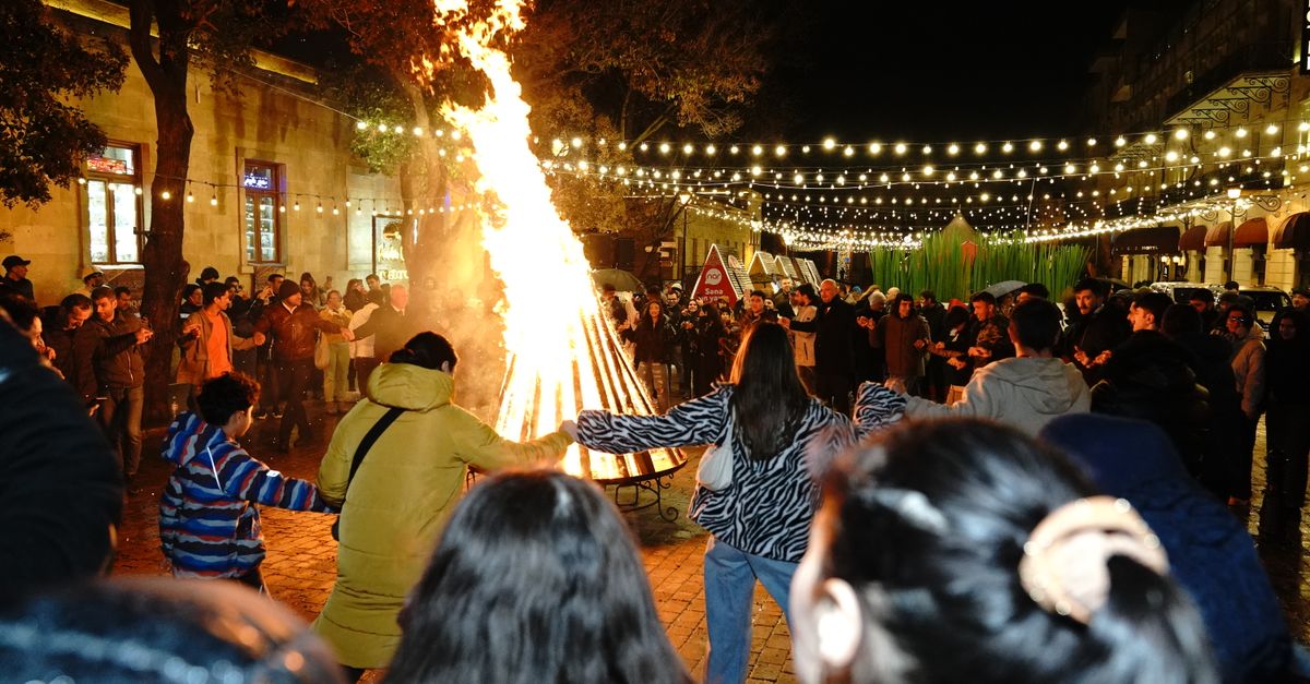 A vibrant night celebration with people dancing around a bonfire under string lights.