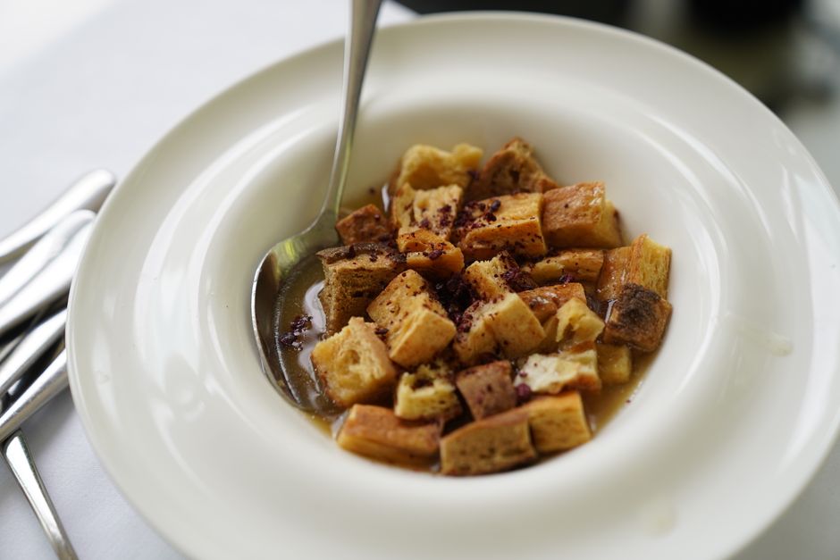 A sheet pan of golden brown crouton cubes tossed with olive oil, garlic, and herbs, next to a bowl of green salad.