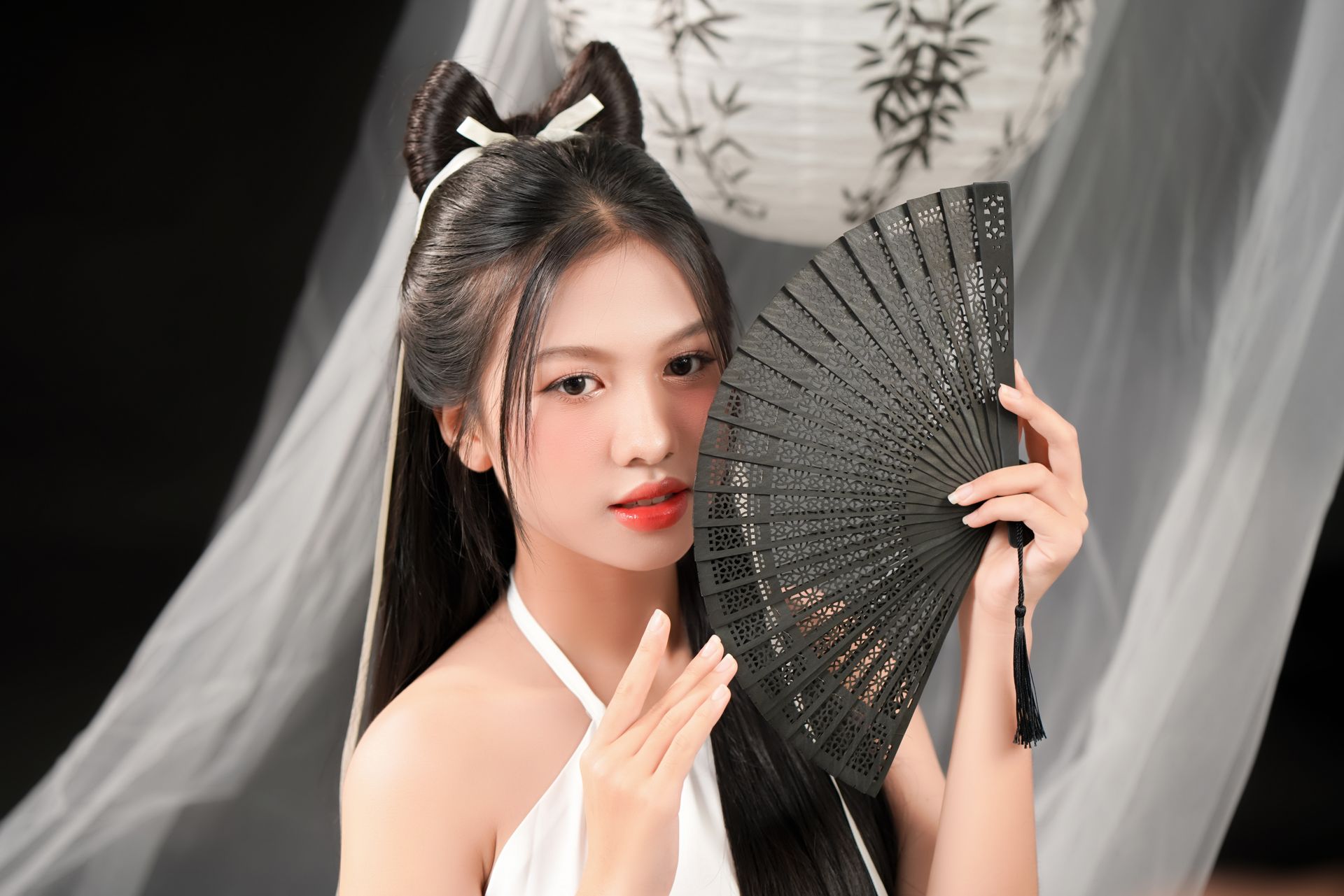 Portrait of a woman holding a traditional fan with Asian decor in a serene setting.