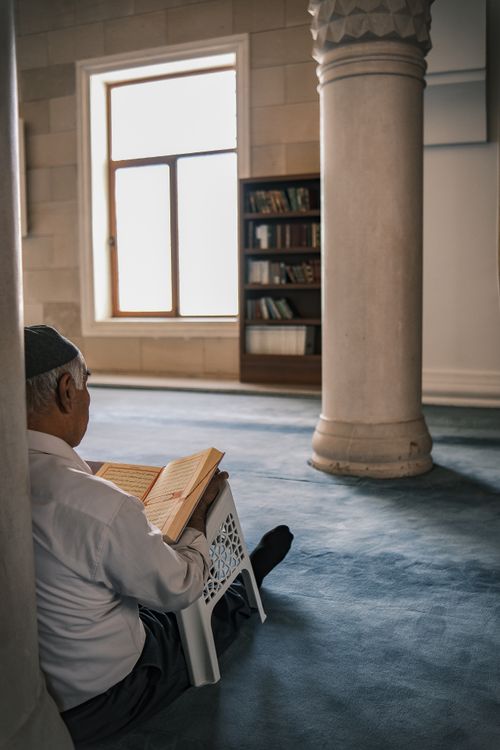 Free An elderly man reads in a peaceful mosque interior, showcasing cultural tradition. Stock Photo
