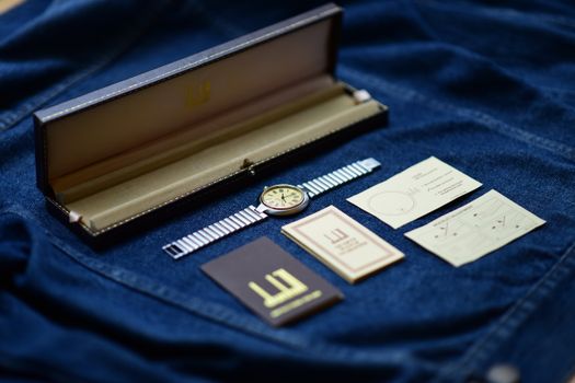Stylish wristwatch with case and instructions displayed on blue denim fabric.