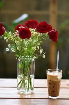 Charming red roses in a vase alongside an iced coffee on a wooden table.