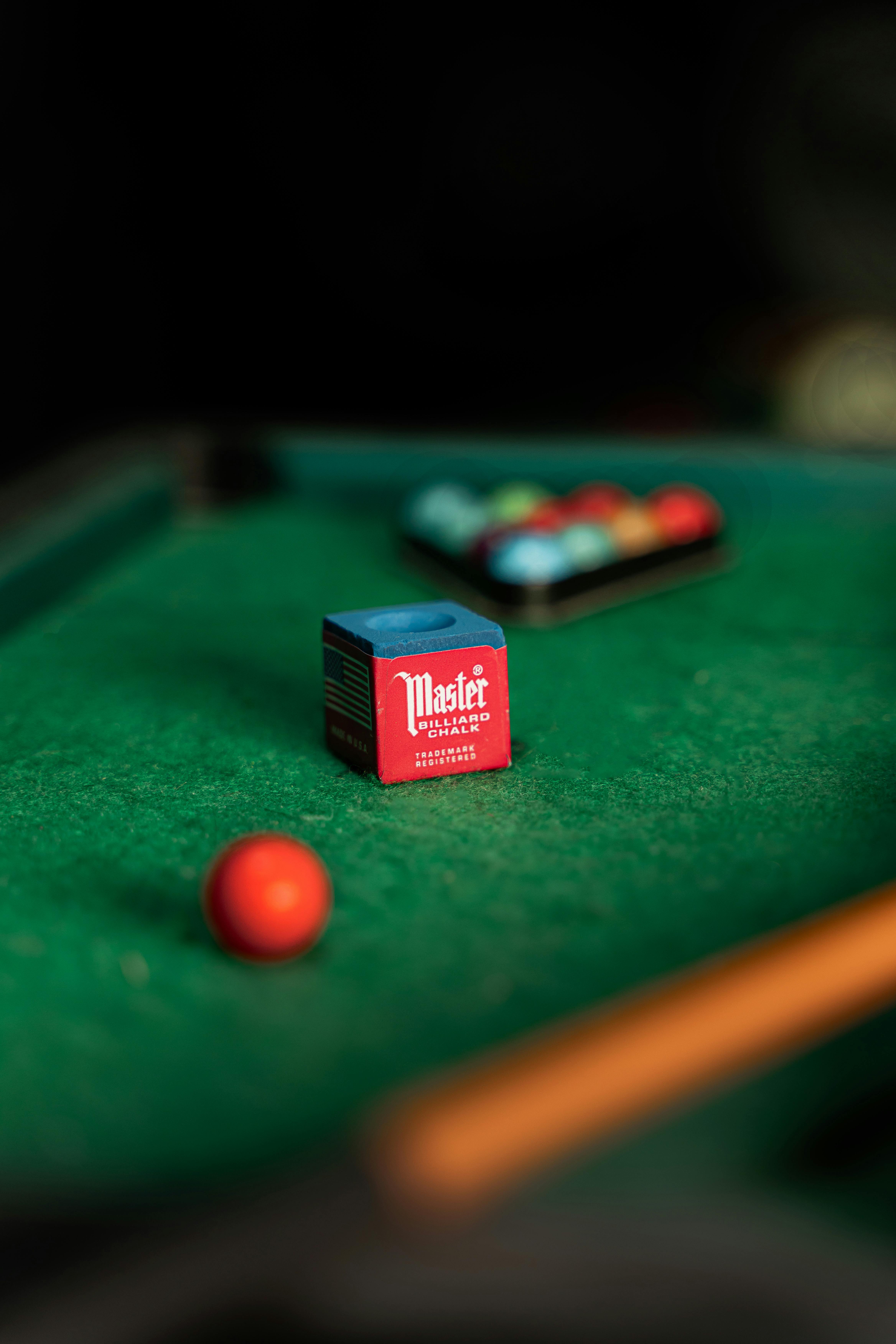 Close-up of a billiard table with chalk cube and red cue ball in focus, perfect for pool enthusiasts.